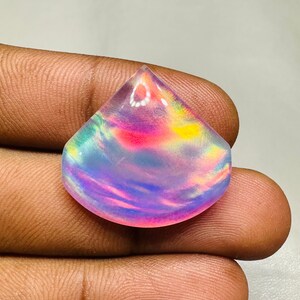 May include: A teardrop-shaped iridescent opal cabochon with a rainbow of colors, including pink, blue, green, and yellow.