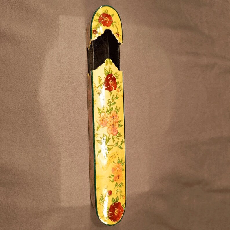May include: A yellow pencil holder with a floral design. The holder is made of wood and has a green trim. The flowers are red, orange, and yellow.