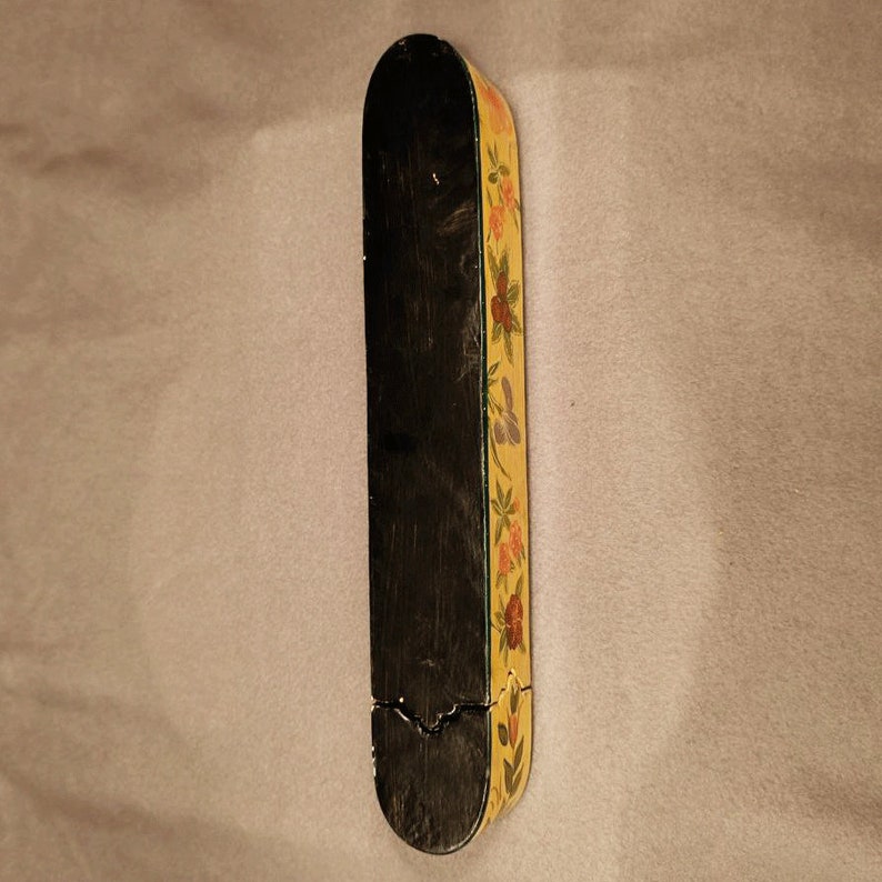 May include: A wooden box with a black interior and a yellow exterior with a floral design. The box is closed.