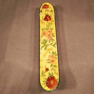 Könnte beinhalten: Eine gelbe Holzkiste mit einem Blumendesign. Die Kiste ist mit roten, rosa und gelben Blumen sowie kleinen gelben Vögeln verziert. Die Kiste hat einen grünen Rand.