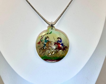 May include: A silver chain necklace with a round, white shell pendant. The pendant is painted with a scene of two people riding horses, with a green background and a few small birds.