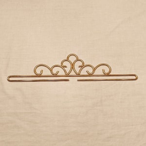 Könnte beinhalten: Eine goldene, kronenförmige Gardinenstange mit dekorativem Design.