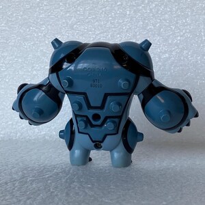 May include: A blue and black plastic toy figure with a stylized, robotic design. The figure has a rounded body with protruding details and black accents. The text "OCII B-10 CHINA 971 80010" is printed on the back.