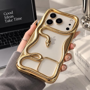 Op de afbeelding: Een transparant telefoonhoesje met een metallic gouden frame en een driedimensionale gouden slang die rond de cameramodule en het achterpaneel is gewikkeld. De slang heeft een textuur met schubben en een gladde kop.