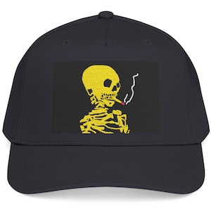 Peut inclure: Une casquette de baseball noire avec un motif rectangulaire sur le panneau avant. Le motif représente un squelette jaune fumant une cigarette avec un bout rouge et de la fumée blanche s'élevant sur un fond gris foncé. La casquette a une visière courbée.