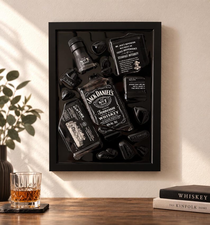 Puede incluir: Una pieza de arte mural con marco negro que presenta una botella de whisky Jack Daniel's Tennessee deconstruida y elementos de etiqueta dispuestos sobre un fondo negro brillante. Incluye el cuello de la botella, la etiqueta principal y paneles de texto.