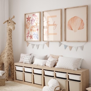 May include: A child's room with framed prints of seashells and a name. A woven giraffe and a storage bench with pillows and storage bins are also present. The art has a neutral colour palette with a beach theme.