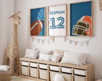 May include: Three framed prints with a blue background. The left print features a football and a sun. The middle print has the name "STEPHAN" and the number "12" in a blue and white striped font. The right print shows a brown and orange football helmet. The prints are hanging on a white wall above a wooden shelf with storage bins.