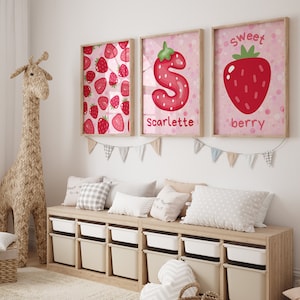 Op de afbeelding: Drie ingelijste prints met een roze achtergrond en witte stippen. De prints tonen een aardbeienpatroon, de letter "S" gemaakt van aardbeien en een hele aardbei met de woorden "Sweet berry".