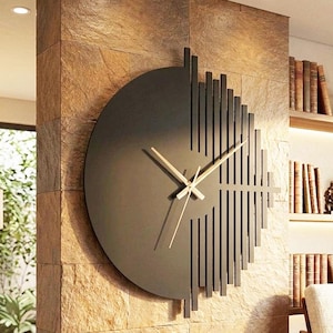 Könnte beinhalten: Eine große, runde Wanduhr mit einer massiven, mattschwarzen linken Hälfte und einer rechten Seite aus vertikalen, schwarzen Lamellen unterschiedlicher Länge. Die Uhr hat dünne, helle Metallzeiger, die mittig auf dem Zifferblatt sitzen.