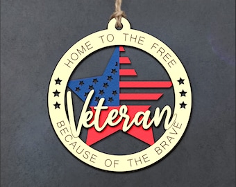 May include: A wooden ornament in the shape of a circle with a star inside. The star is red, white, and blue and has the word "Veteran" written in cursive on it. The circle has the text "Home to the Free Because of the Brave" around the edge.