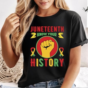 May include: Black t-shirt featuring the text "Juneteenth Know Your History" in red, yellow, and green. The design includes a raised fist inside a red circle, with yellow and green ribbons on either side.