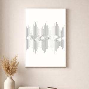 May include: A framed art print featuring a minimalist design of vertical, wavy lines in dark purple against a white background. The artwork is displayed on a light wooden table with decorative items, including a vase with dried plants.