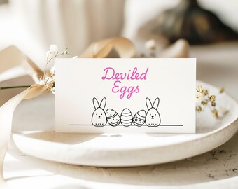 May include: A white card with the text "Deviled Eggs" in pink lettering.  The card has a black and white illustration of four Easter eggs with bunny faces.