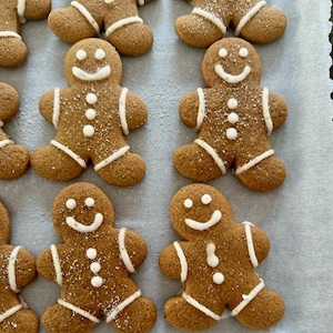 May include: A baking sheet with gingerbread cookies decorated with white icing and sprinkles. The cookies are shaped like gingerbread men and have smiling faces.