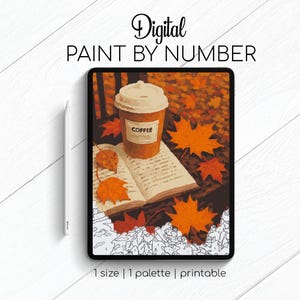 Op de afbeelding: Digitale paint-by-number afbeelding op een tablet. Het kunstwerk toont een koffiekopje, een open boek en herfstbladeren in tinten oranje en bruin. De tablet staat op een wit oppervlak met een stylus. Tekst op de afbeelding luidt "Digital Paint by Number".