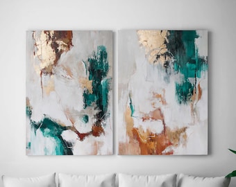 May include: Two abstract paintings with a white background, featuring strokes of teal, brown, and gold leaf accents. The artwork is displayed on a white wall above a white sofa, creating a modern aesthetic.