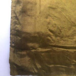Puede incluir: Primer plano de una tela dorada con un ligero brillo. La tela tiene algunos peque&ntilde;os agujeros y est&aacute; ligeramente arrugada.