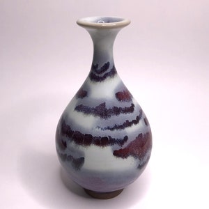 Könnte beinhalten: Eine kleine, weiße Keramikvase mit einer lila und braunen Glasur. Die Vase hat einen runden Körper und einen schmalen Hals.
