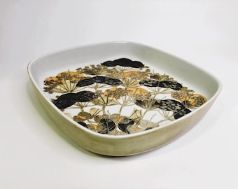 May include: A white ceramic serving dish with a square shape and a raised rim. The dish features a black and brown floral pattern with yellow accents.