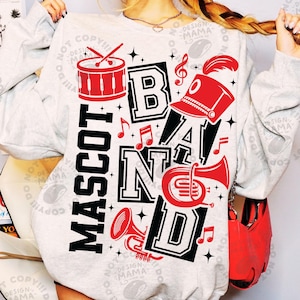 May include: A light grey crewneck sweatshirt featuring a graphic print with the text MASCOT BAND in bold black lettering. The design includes red illustrations of a drum, a marching band hat, a trumpet, a French horn, and musical notes.