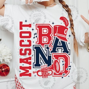 May include: A white short-sleeve t-shirt featuring a graphic design with the red and navy blue text "MASCOT BAND". The design includes a red marching band hat, a red trumpet, and musical notes. The shirt is paired with red and white chequered trousers.