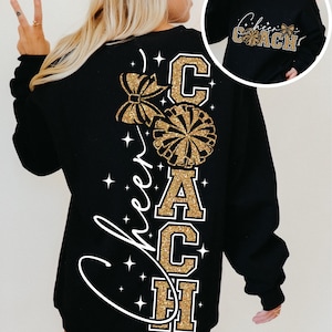 以下が含まれることがあります： ゴールドグリッターの「Cheer Coach」デザインの黒いスウェットシャツ。背面には大きなリボン、ポンポン、ブロック体の「Coach」の文字があります。白い星とスクリプトの「Cheer」の文字がデザインを完成させています。