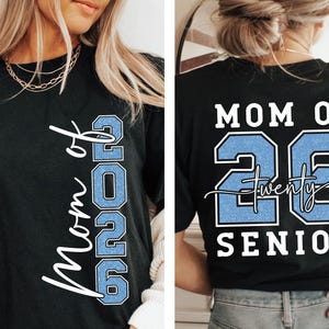 May include: Black t-shirt with the text "Mom of 2026" in white script and the number "2026" in light blue. The back of the shirt reads "Mom of 26 Twenty Senior" in white and light blue.