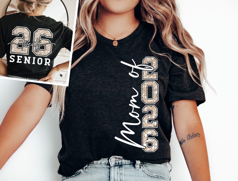 May include: Dark gray t-shirt with the text "Mom of 2026" in white script. The number "2026" is in a glittery, tan font. The back of the shirt in the inset image says "26 Twenty SENIOR" in a similar glittery font.