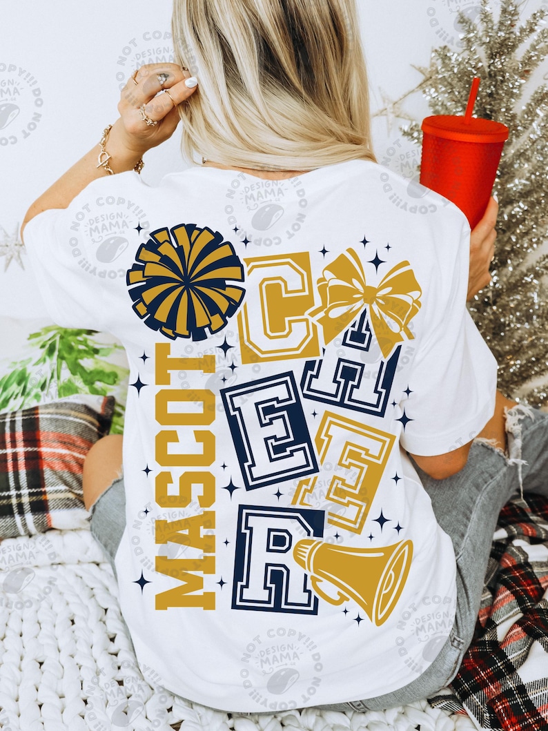 May include: White t-shirt with a cheerleading design. The design includes a pom-pom, bow, megaphone, and the word "MASCOT" vertically. The word "CHEER" is displayed in a collegiate font. The colors are navy blue and gold.