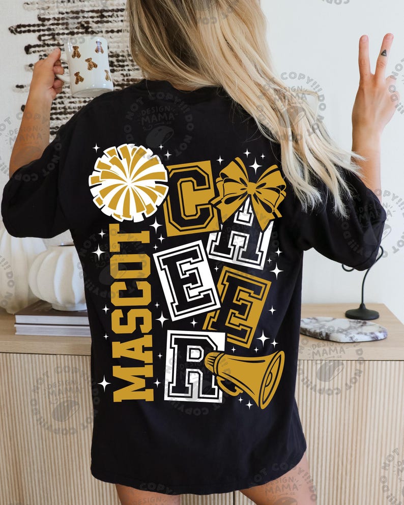 May include: Black t-shirt with a gold and white design. The design includes the words "MASCOT CHEER" in a collegiate font, a pom-pom, a bow, and a megaphone. The shirt is a casual style.