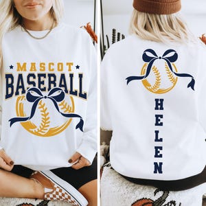 Peut inclure: Sweat-shirt blanc avec un motif de baseball. Le devant affiche "MASCOT BASEBALL" en bleu marine et or, avec un graphisme de baseball et de ruban. Le dos pr&eacute;sente un graphisme de baseball avec un n&oelig;ud bleu marine et le nom "HELEN" en bleu marine.