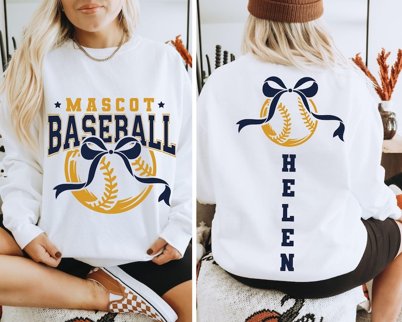 Peut inclure: Sweat-shirt blanc avec un motif de baseball. Le devant affiche "MASCOT BASEBALL" en bleu marine et or, avec un graphisme de baseball et de ruban. Le dos pr&eacute;sente un graphisme de baseball avec un n&oelig;ud bleu marine et le nom "HELEN" en bleu marine.