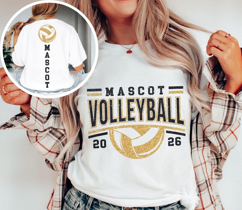 Op de afbeelding: Wit T-shirt met "MASCOT VOLLEYBALL" in zwarte en gouden glitterletters. Een gouden volleybalafbeelding staat onder de tekst, met de jaartallen "20" en "26" aan weerszijden. De achterkant van het shirt heeft een volleybalafbeelding en het woord "MASCOT" in zwart.