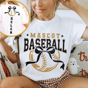 Peut inclure: T-shirt blanc avec l'inscription "MASCOT BASEBALL" en noir et or, un graphisme de baseball et un n&oelig;ud noir. Le dos du t-shirt montre un graphisme de baseball avec un n&oelig;ud noir et le nom "HELEN" en noir.