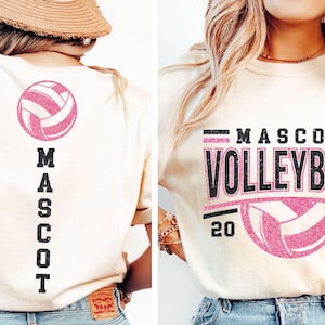 Op de afbeelding: Cr&egrave;mekleurig T-shirt met een roze volleybalafbeelding. De voorkant van het shirt heeft de woorden "MASCOT VOLLEYBALL 20 26". De achterkant van het shirt heeft een volleybal en het woord "MASCOT" verticaal.