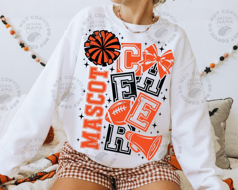 May include: A white long-sleeve sweatshirt featuring a graphic print in orange and black. The design includes the word MASCOT vertically, the word CHEER in block letters, a pom-pom, a hair bow, a football, and a megaphone with star accents.
