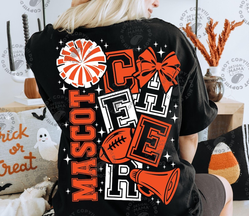 May include: A black t-shirt featuring a large graphic on the back with the word CHEER in bold block letters, a pom-pom, a hair bow, a football, and a megaphone. The design includes the word MASCOT in orange and white, accented by stars.