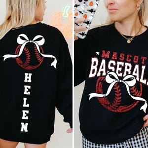 Peut inclure: Sweat-shirt noir avec un motif de baseball. Il pr&eacute;sente une balle de baseball rouge paillet&eacute;e, un n&oelig;ud blanc et le texte "MASCOT BASEBALL". Le dos du sweat-shirt porte le nom "HELEN" en blanc.