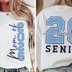 May include: White t-shirt with "Mom of 2026" in vertical blue text. A white sweatshirt with "26 Twenty Senior" in blue glitter text. Both items are likely for a graduation theme.