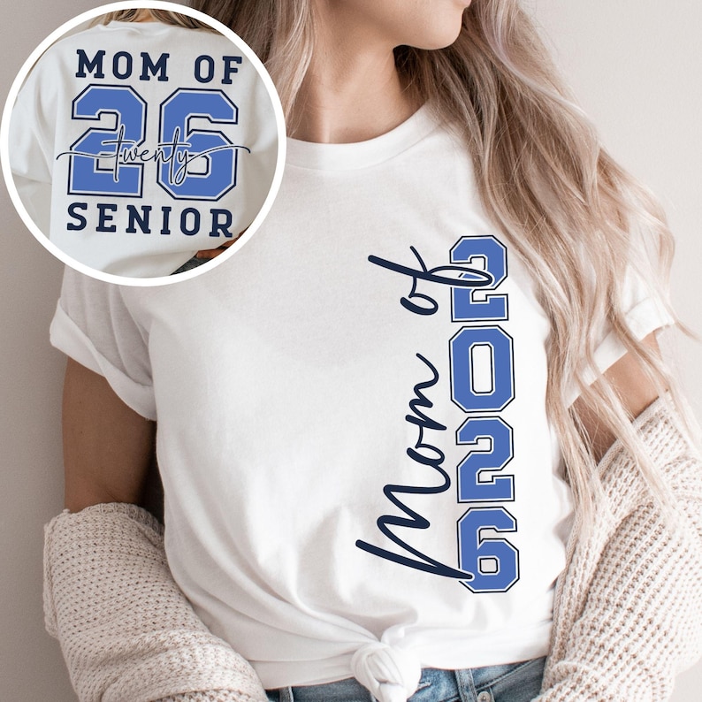 May include: White t-shirt with the text "Mom of 2026 Senior" in blue. The number "26" is in a bold, blocky font, and "Twenty" is written in a script font. The shirt is tied at the waist.