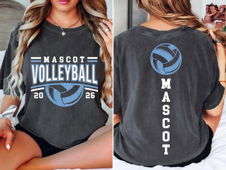 Op de afbeelding: Donkergrijs t-shirt met "MASCOT VOLLEYBALL" in wit en lichtblauw, een volleybalafbeelding en de jaren 20 en 26. De achterkant van het shirt heeft een volleybalafbeelding en het woord "MASCOT" verticaal.