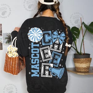 May include: Black long-sleeve sweatshirt with a cheerleading design. The design includes the words "MASCOT CHEER" in white and light blue, along with a pom-pom, bow, and megaphone graphic. The sweatshirt has white stripes on the sleeves.