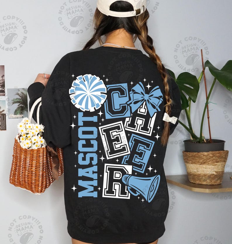 May include: Black long-sleeve sweatshirt with a cheerleading design. The design includes the words "MASCOT CHEER" in white and light blue, along with a pom-pom, bow, and megaphone graphic. The sweatshirt has white stripes on the sleeves.