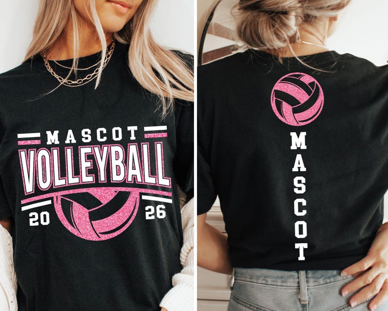 Op de afbeelding: Zwart t-shirt met "MASCOT VOLLEYBALL 20 26" in witte en roze letters, met een volleybalafbeelding. De achterkant van het shirt toont een roze volleybal en het woord "MASCOT" verticaal.