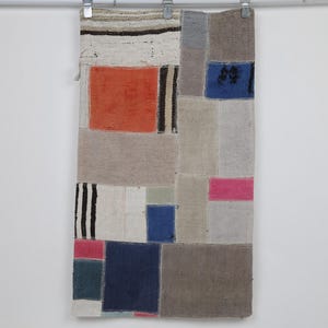 May include: A rectangular textile wall hanging featuring a patchwork design of various fabric segments in shades of orange, blue, pink, gray, beige, and white, with some sections displaying black and white striped patterns and solid color blocks.