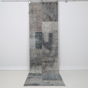 May include: A long rectangular runner rug featuring a patchwork design composed of various gray, blue, and muted brown fabric sections. The rug displays a distressed, weathered texture with visible stitched seams connecting the different patterned panels.