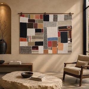 May include: A large rectangular wall hanging composed of various fabric patches in shades of black, white, red, orange, blue, and grey. The textile features a geometric patchwork design and is suspended from a horizontal wooden rod mounted on the wall.