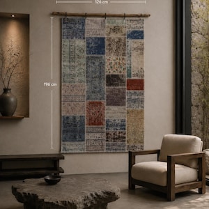 Puede incluir: Un tapiz de pared rectangular de estilo patchwork con varios patrones descoloridos en tonos azul, rojo, marrón y crema. El tapiz cuelga de una vara de madera y mide 126 cm de ancho por 196 cm de alto, mostrando costuras visibles.