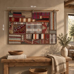 May include: A rectangular wall hanging tapestry featuring a patchwork of various woven fabric patterns in shades of red, brown, gray, and white. The tapestry is suspended from a wooden rod and measures 90 cm in width by 60 cm in height.